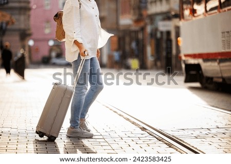 Woman tourist pulling suitcase and walks across street with tram tracks in city. Travel and vacation lifestyle