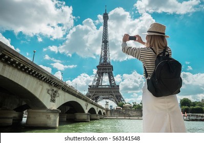 Woman Tourist Selfie Near The Eiffel Tower In Paris Under Sunlight And Blue Sky. Famous Popular Touristic Place In The World.