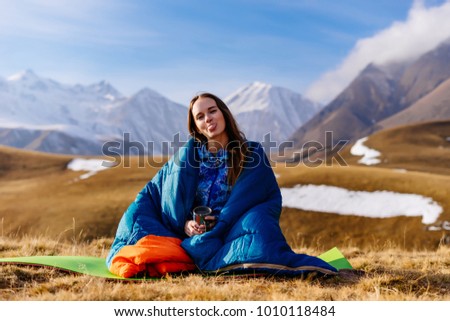 woman tourist sits and shows tongue against the background of high mountains