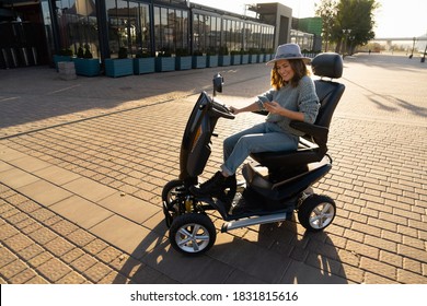 Woman tourist with smartphone on a four wheel mobility electric scooter on a city street.	