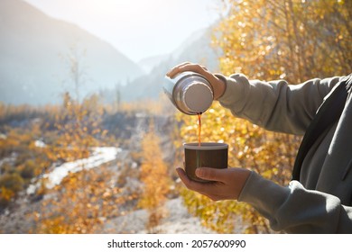 Woman tourist with thermos and cup with coffee in autumn lake camping in the mountains. Preparing coffee outdoor concept 