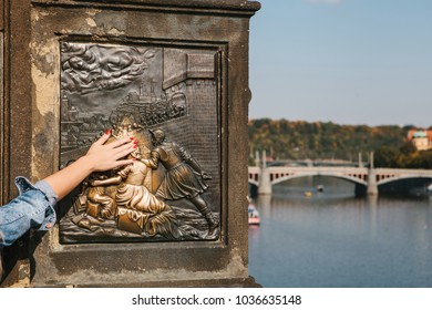 Woman tourist touches a bronze statue of John of Nepomuk on the Charles bridge in Prague, Czech Republic for good luck. Legends.