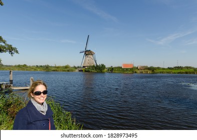 Woman tourist travelling in Holland in front of Dutch windmill, navy jacket, red bag, blue sky and beautiful weather