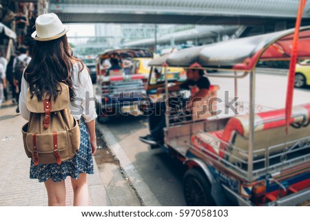 Woman tourist walking in busy bangkok street on thailand travel. Asian girl on street during Asia summer vacation. Thai traditional taxi tuk tuk car.