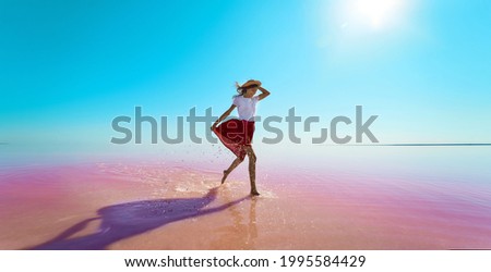 Woman tourist walking on bright pink water, calm water surface of lake and blue sky