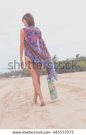 Woman tourist walking on a tropical summer vacation beach wearing sunglasses and beach bag relaxing on travel holidays. Young lady in luxury fashion beachwear, Bali island, Indonesia.