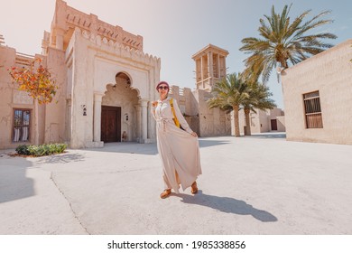 Woman tourist wearing red turban and biege long dress walks through the old narrow streets of Bur Dubai and Creek. Travel and sightseeing concept