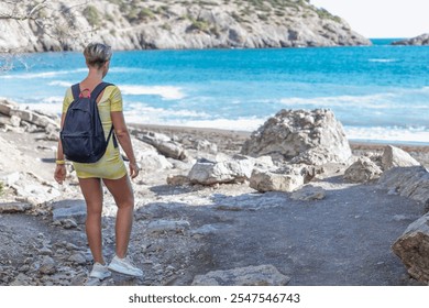 Woman tourist in yellow mini dress with backpack on rocky beach in the mountains. Rest and relaxation. Beautiful landscape. - Powered by Shutterstock