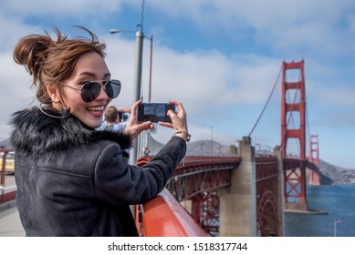 Woman Tourists use smartphone  take a photo visiting the world-famous Golden Gate Bridge of San Francisco in California America.Travel Lifestyle and vacation concept. - Powered by Shutterstock