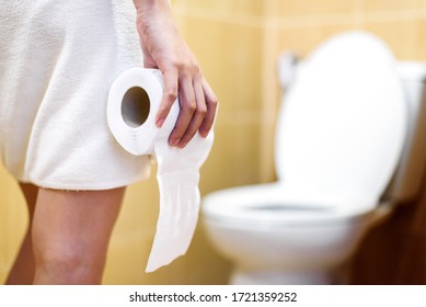 woman in towel holding toilet tissue paper roll in restroom