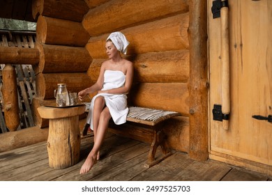 Woman with towel on her head drinking herbal tea after spa procedures. Wellness spa. Young woman relaxing sauna wrapped in towel. Girl Sauna. Wooden steam room. Russian bathroom. Relax Bathhouse - Powered by Shutterstock