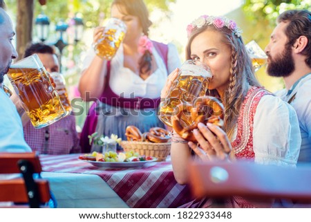 Woman in Tracht looking into camera while drinking a mass of beer surrounded by her friends