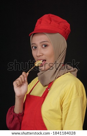 a woman trader in full uniform, is promoting her food in the form of egg satay. The woman bites and eats eggs to show off its delicacy.	
