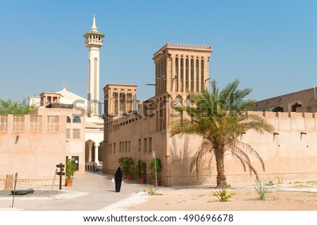 Woman in traditional muslim black dress in old arabic city district with mosque minaret on background