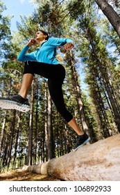 Woman Trail Running In The Woods And Jumping Over Logs While On Extreme Outdoor Fitness Training In Forest.