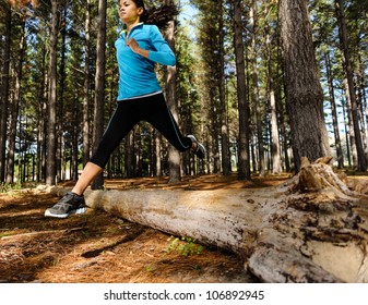 Woman Trail Running In The Woods And Jumping Over Logs While On Extreme Outdoor Fitness Training In Forest.