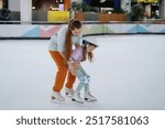 Woman trainer teaches figure skating on ice. Protective ammunition: helmet, knee pads and elbow pads. Selective focus, blurred background.