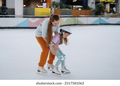 Woman trainer teaches figure skating on ice. Protective ammunition: helmet, knee pads and elbow pads. Selective focus, blurred background.