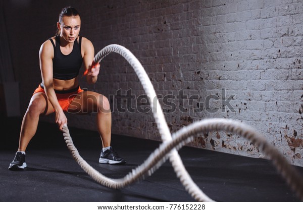 Woman training\
with battle rope in cross fit\
gym