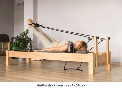 Woman training pilates on the reformer bed. Reformer pilates studio machine for fitness workouts in gym. Fit, healthy and strong authentical body. Fitness concept - Shutterstock ID 2284764029