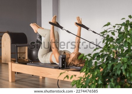 Woman training pilates on the reformer bed. Reformer pilates studio machine for fitness workouts in gym. Fit, healthy and strong authentical body. Fitness concept