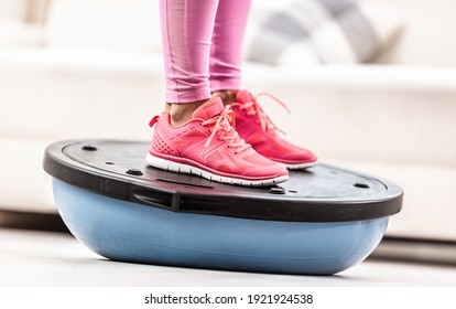 Woman in training shoes stands on a blue balance ball.