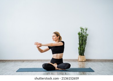 A woman trains sitting on a yoga mat, stretching her arm to the side, stretching muscles during training, preparing the body for exercises. High quality photo