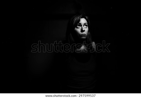 A woman trapped in the dark looking up into a shaft\
of light