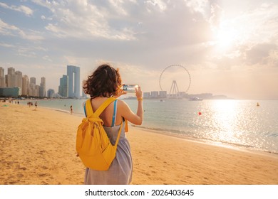 Woman travel blogger takes pictures for social networks of skyscrapers on Bluewaters island and the famous Ain Ferris Wheel in Dubai