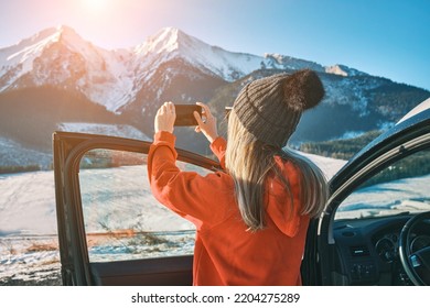 Woman travel exploring, enjoying the view of the mountains, landscape, lifestyle concept winter vacation outdoors. Female with mobile phone standing near the car in sunny day. - Shutterstock ID 2204275289