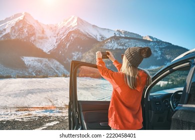 Woman travel exploring, enjoying the view of the mountains, landscape, lifestyle concept winter vacation outdoors. Female with mobile phone standing near the car in sunny day. - Shutterstock ID 2220458401