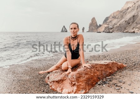 Woman travel portrait. Happy woman with long hair looking at camera and smiling. Close up portrait cute woman in black bikini posing on a red volcanic rock on the sea beach