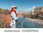 A woman traveler checks her map on smartphone app while standing on a bridge in Podgorica, Montenegro, navigating the city with focus and curiosity.