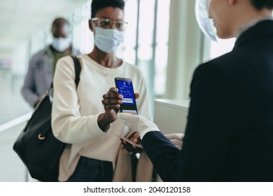 Woman traveler in face mask showing boarding pass at check-in counter at airport. Female in pandemic with digital air ticket at airport.