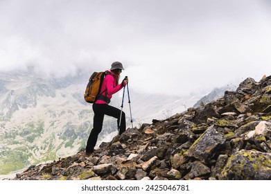 Una mujer viajera va a la cima de la montaña. Una niña con bastones de trekking y una mochila se detuvo a admirar la niebla que se le acercaba en las montañas