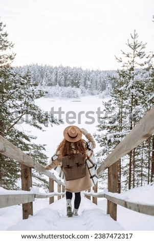 Woman traveler in a hat with a backpack on a wooden ladder. Young woman enjoying winter nature on a sunny day. Active lifestyle. Travel concept.