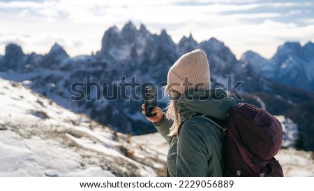 Woman traveler making photo with her smartphone in Tre Cime di Lavaredo in snow South Tyrol, Italy. Winter landscape of Dolomites, Italy