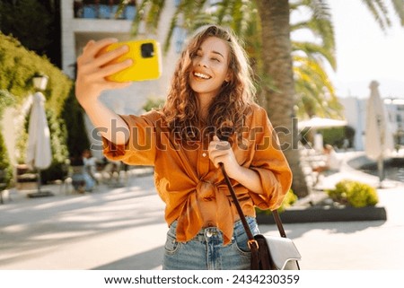 Woman traveler with a mobile phone, takes a selfie, communicates via video link  near palm tree  for a travel blog. Adventure, vacation concept.