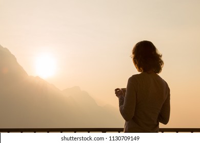 Woman traveler silhouette starting new day enjoying morning coffee looking at peaceful serene sunrise on morning sky watching sunlight above mountains landscape relaxing on travel vacation, rear view - Powered by Shutterstock