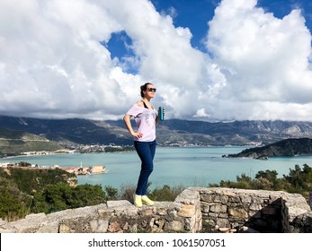 Woman traveler standing on wall on the ruins of medieval fortress Mogren at the shore of Adriatic sea. Girl has thermos and drinks 