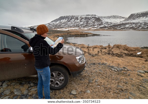 Woman traveler steps out\
of 4x4 rental car on holiday and looks at map, solo adventure\
roadtrip holiday