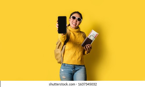 Woman Traveler With Suitcase, Holding Passport And Ticket In The Hand, And Submit Mobile Phones Coming In Front Of The Camera On Yellow Background. Travel Backpack