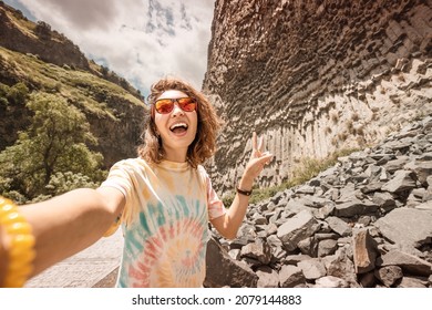 Woman traveler takes selfie photo on mobile phone at the basalt columns or a symphony of stones resembles a musical organ in Garni, Armenia
