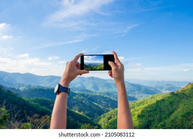A woman traveler uses her smartphone to photograph a mountain landscape. Stop along the way to take photos and share them on social media.