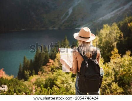 Woman traveler wearing hat and looking at amazing mountains and lake, wanderlust travel concept. Lake Morskoy Eye in the Polish Tatras.
