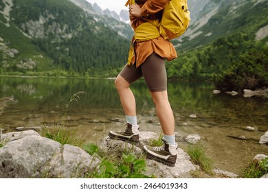 Woman traveler with yellow hiking backpack and hiking stiks enjoys the scenery. Active lifestyle. Wanderlust. - Powered by Shutterstock