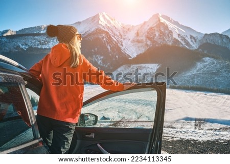 Woman traveling exploring, enjoying the view of the mountains, landscape, lifestyle concept winter vacation outdoors. Female standing near the car in sunny day, travel in the mountains.