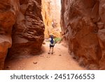 Woman Traveling through Narrow Sandstone Desert Rock Canyon Hiking Trail in Fiery Furnace, Arches National Park, Utah, United States