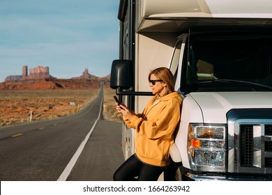 A woman travels by motorhome through Monument Valley in the USA desert and checks her mobile phone parked on the side of the road - Powered by Shutterstock