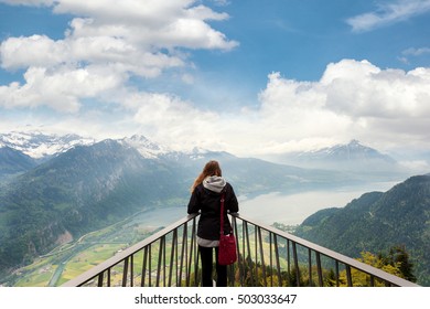 Woman Traverler Looking Aerial View Of The City District And Interlaken From Viewpoint At Harder Kulm In Interlaken, Bern, Switzerland.